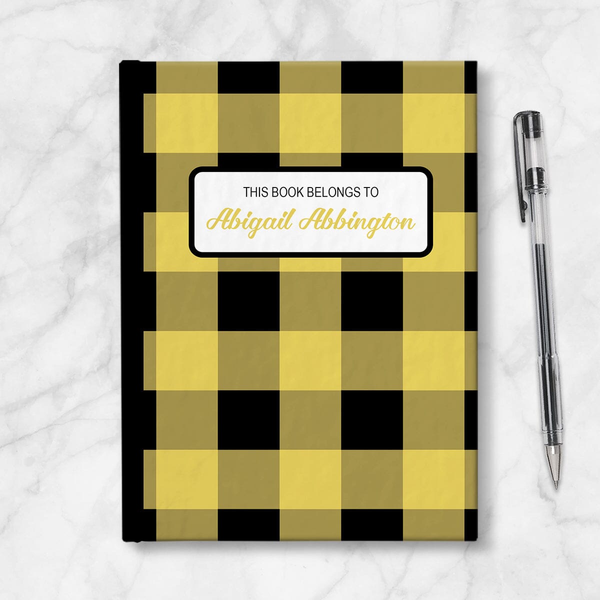 Personalized Yellow and Black Buffalo Plaid Journal at Artistically Invited. Image shows the book on a countertop next to a pen.