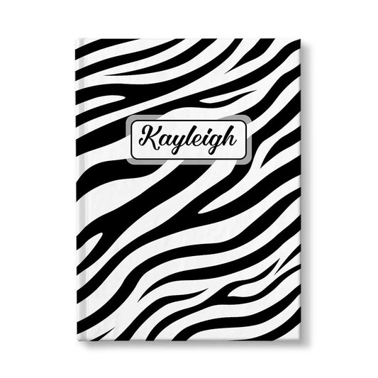 Personalized Zebra Print Journal at Artistically Invited. A custom book illustrated with a bold and sleek black and white zebra print pattern that wraps around the cover of the journal. Your personalized name is custom printed in a cute script font in black within a white rectangular design on the front of the book over the zebra print background.